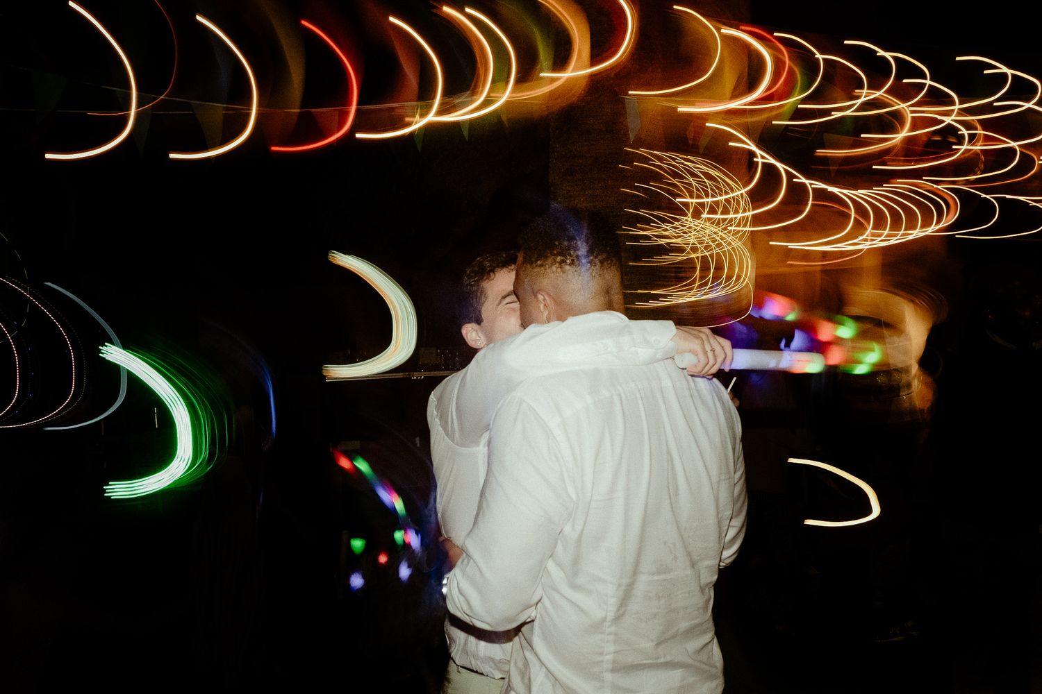 Couple embracing at night with colorful light trails swirling around them in a long exposure wedding photo.