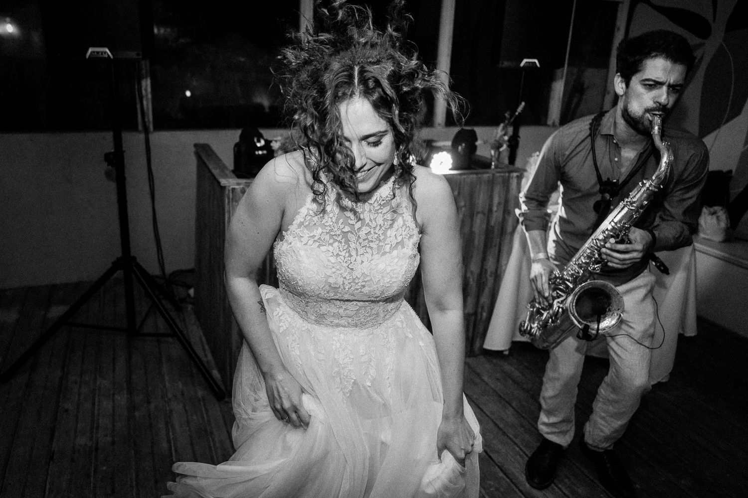 Black and white photo of a bride dancing joyfully while a saxophonist performs at an elegant wedding reception.