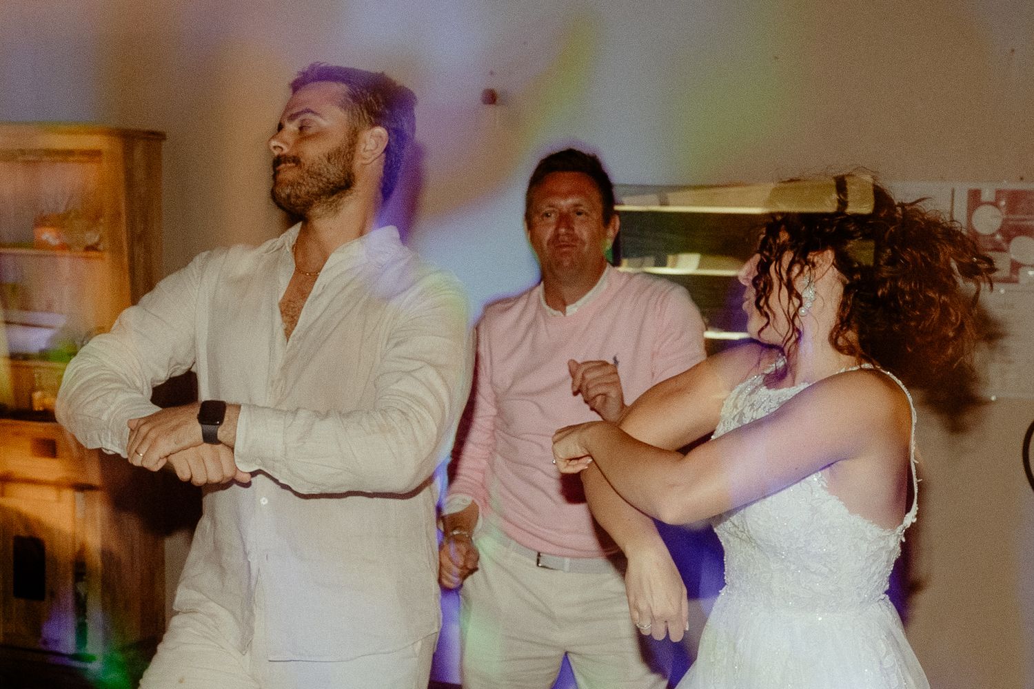 Three guests dancing joyfully under purple lights at a lively wedding reception party.