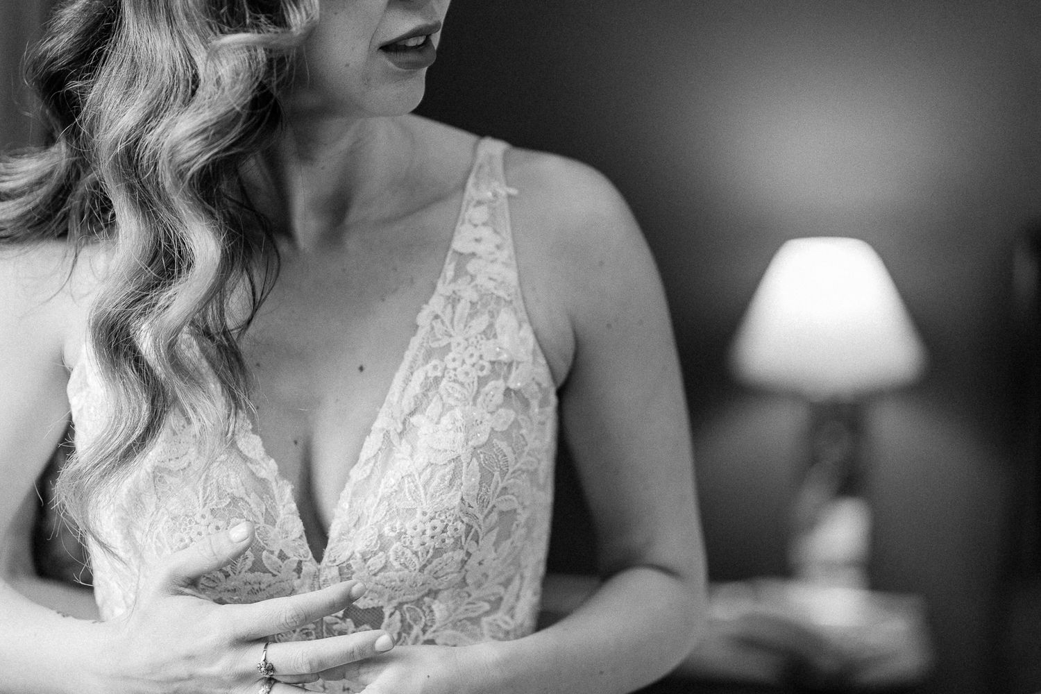 Black and white photo of a bride in a lace wedding dress, soft lighting with a lamp in the background.