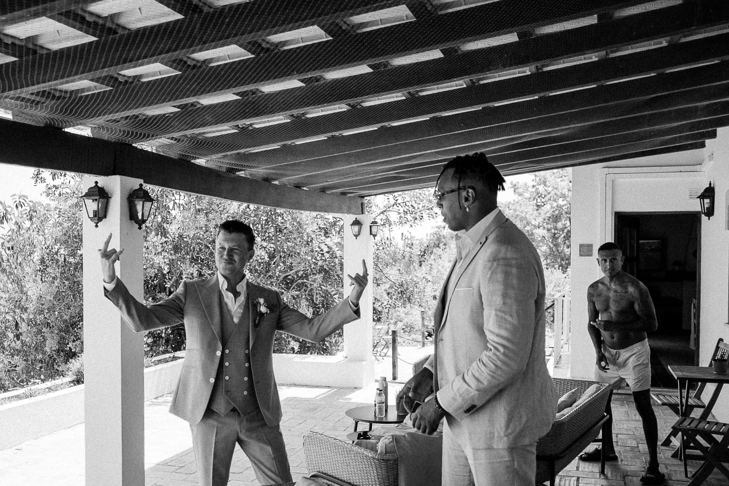 Two men in suits toasting drinks on a covered outdoor patio in black and white wedding photo.