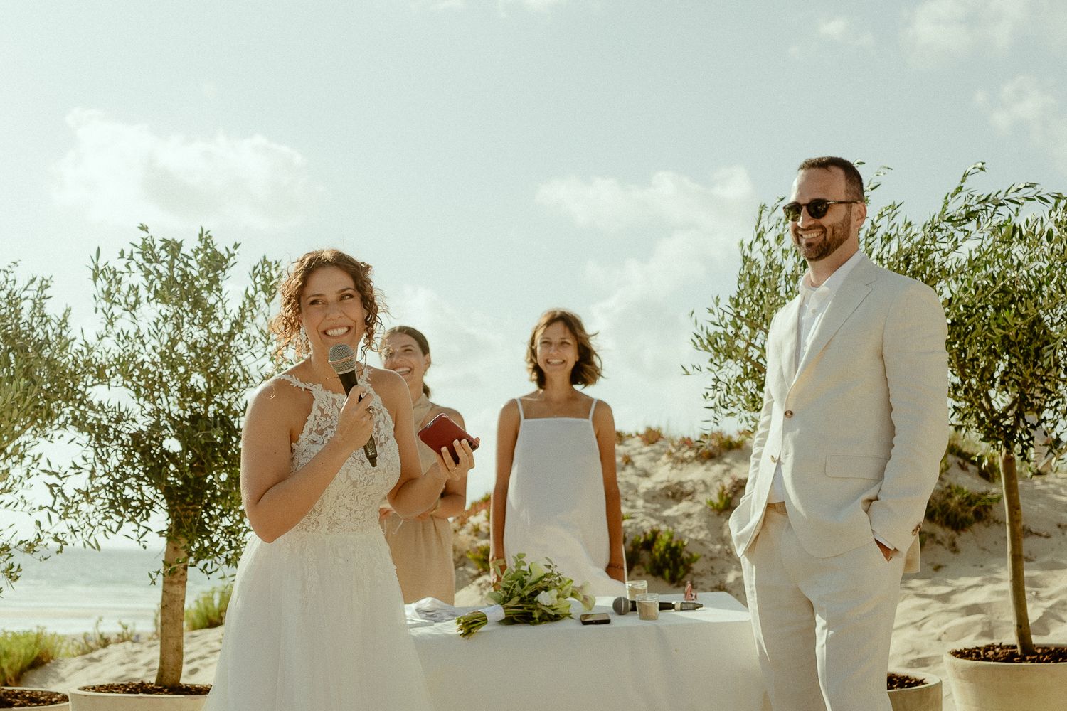Bride and groom exchange vows at a romantic outdoor beach wedding ceremony with guests and greenery.