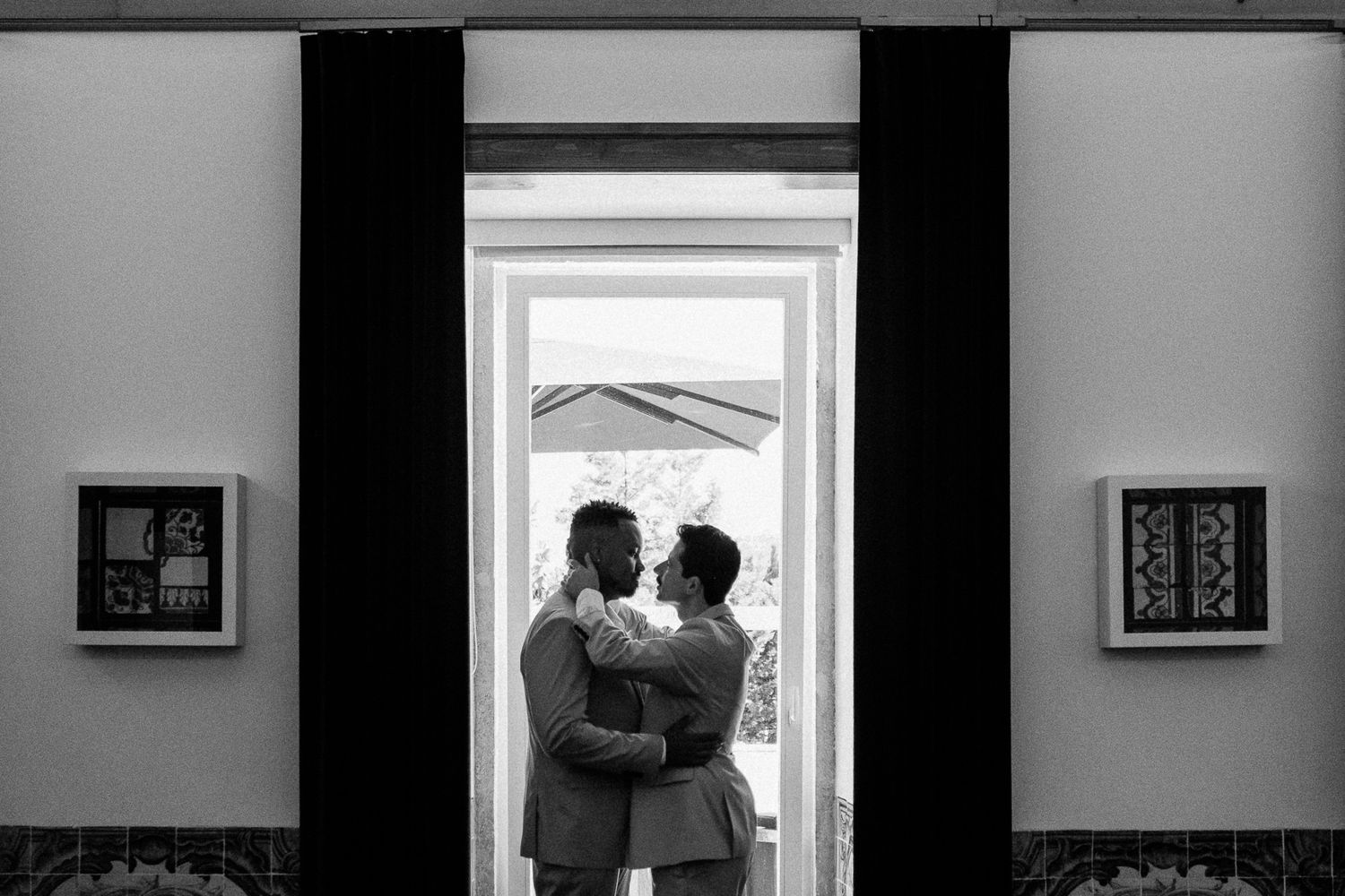 Black and white photo of two grooms embracing in a doorway on their wedding day.