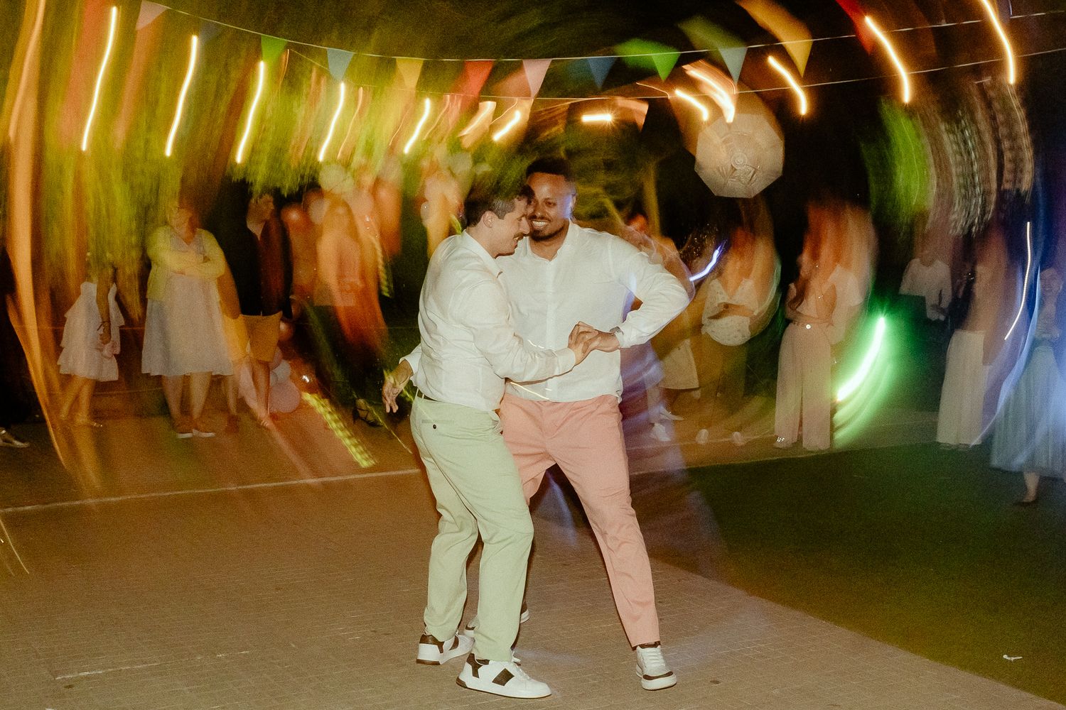 Two people dancing joyfully at a colorful neon-lit party event with motion blur effect.