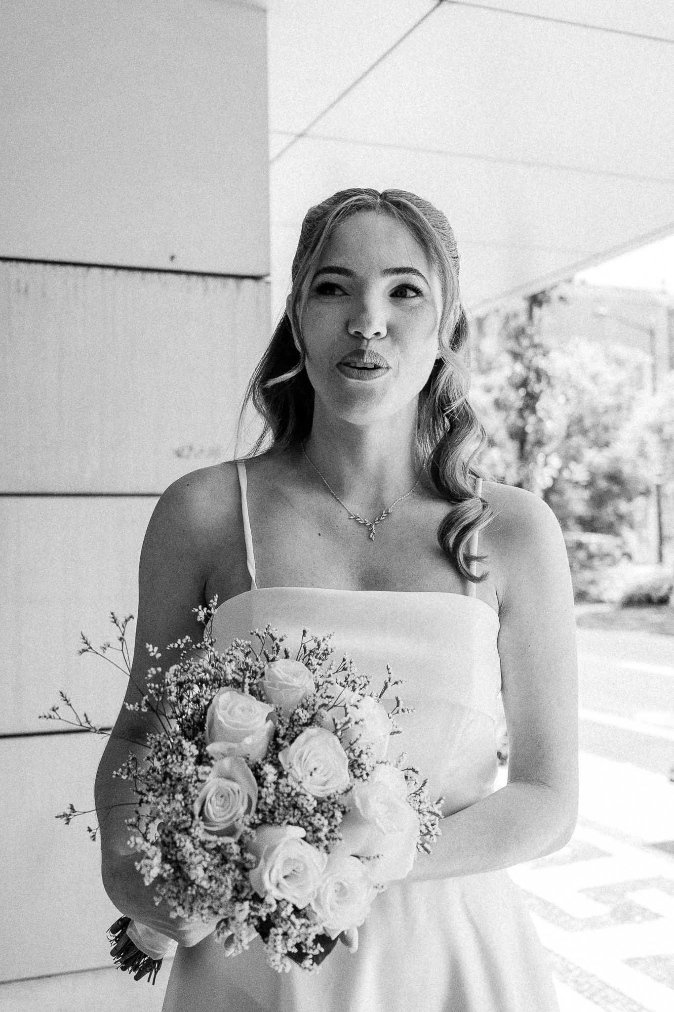 Black and white photo of a bride in a white dress holding a bouquet of roses and wildflowers.