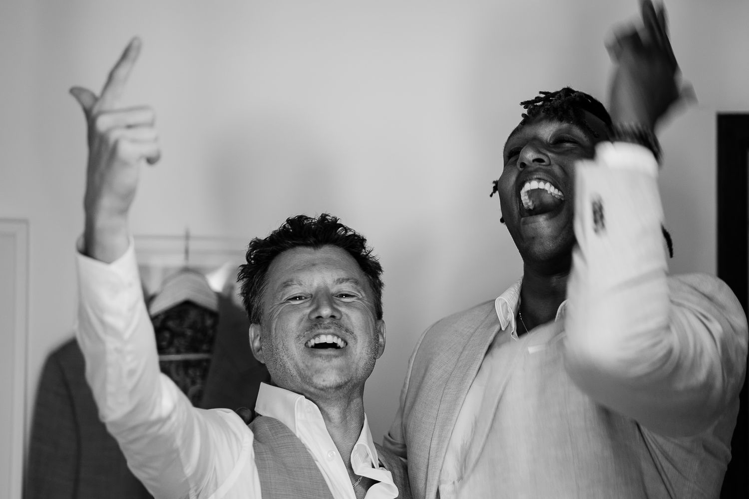 Two men laughing and celebrating joyfully, raising hands in excitement, captured in black and white photography.