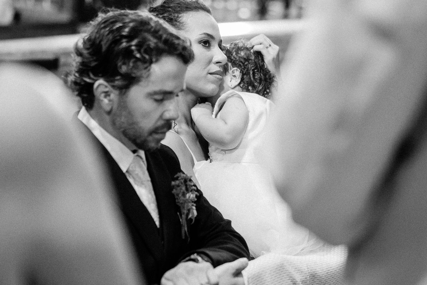Black and white wedding photo of a groom and bride holding a young girl in a white dress during the ceremony.