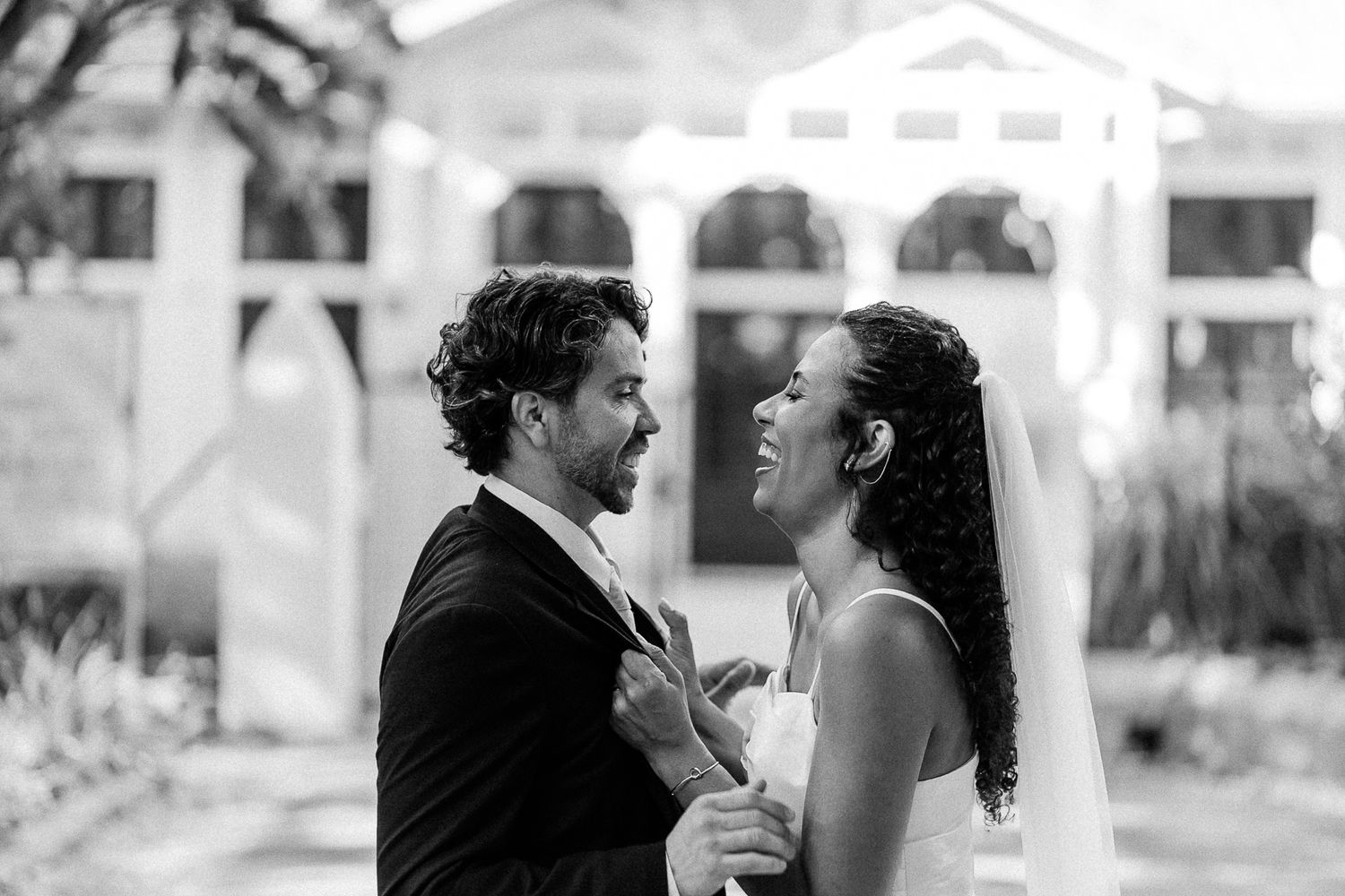 Black and white photo of a bride and groom sharing a joyful moment outdoors at their wedding venue.