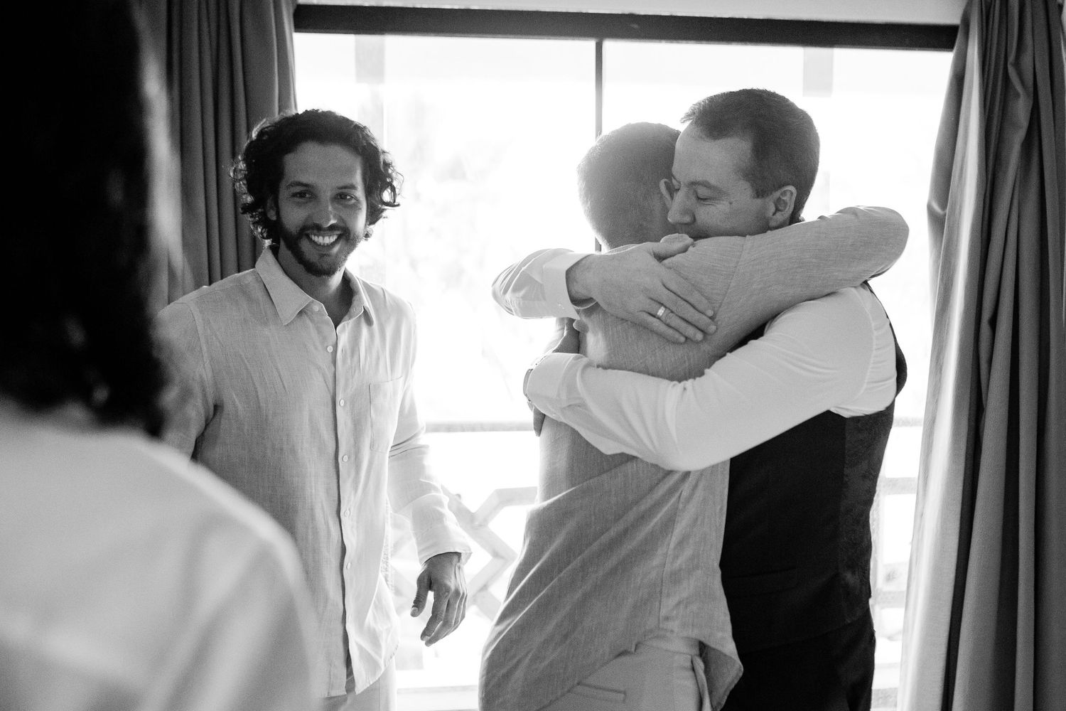 Black and white photo of joyful people embracing and celebrating in a bright sunlit room.