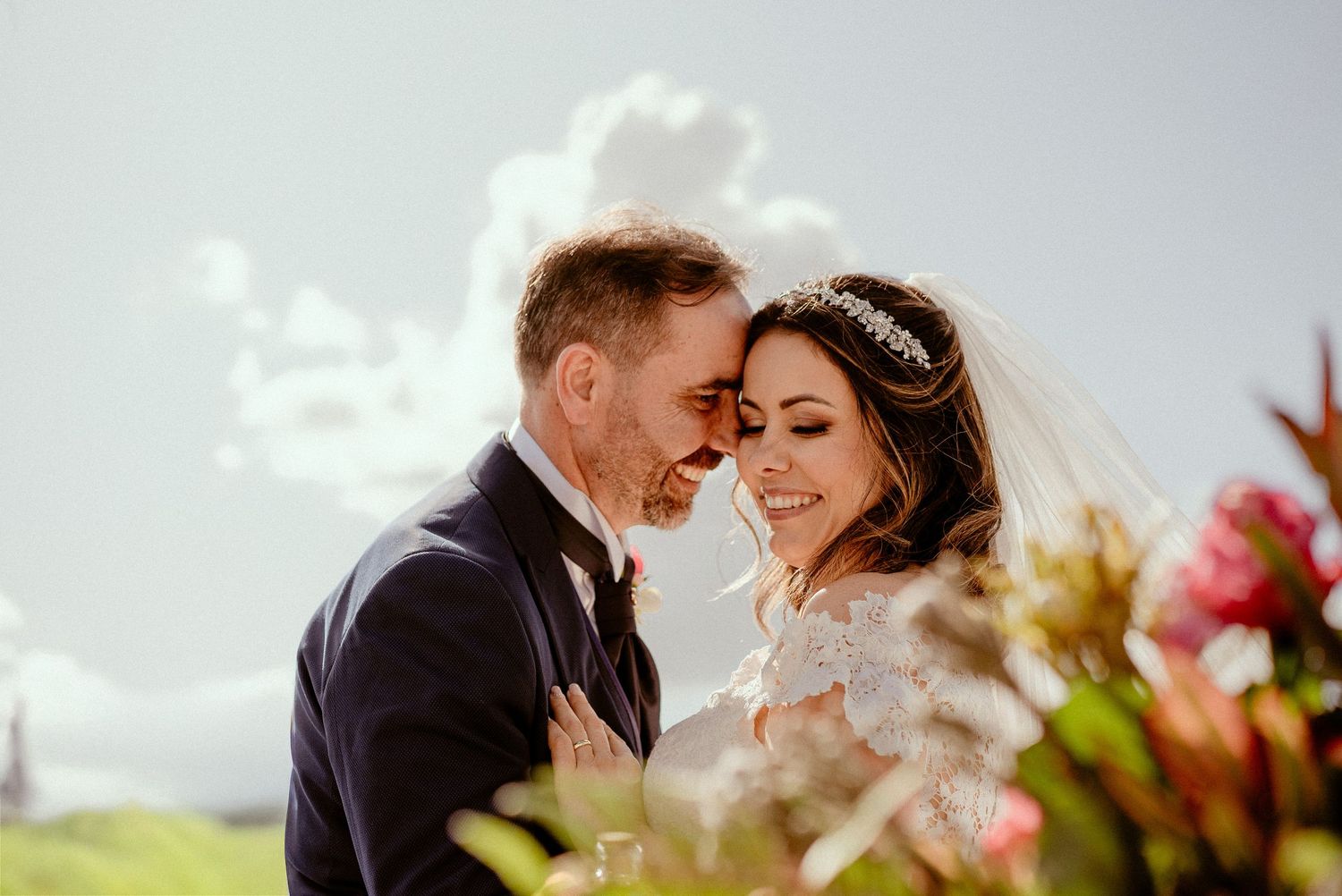 A romantic wedding couple embraces in a sunlit outdoor setting during their special day.