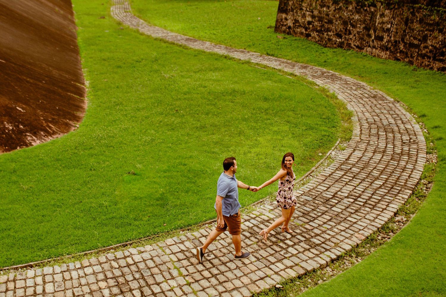 Children walk along a curved brick path through a lush green lawn in a garden setting.