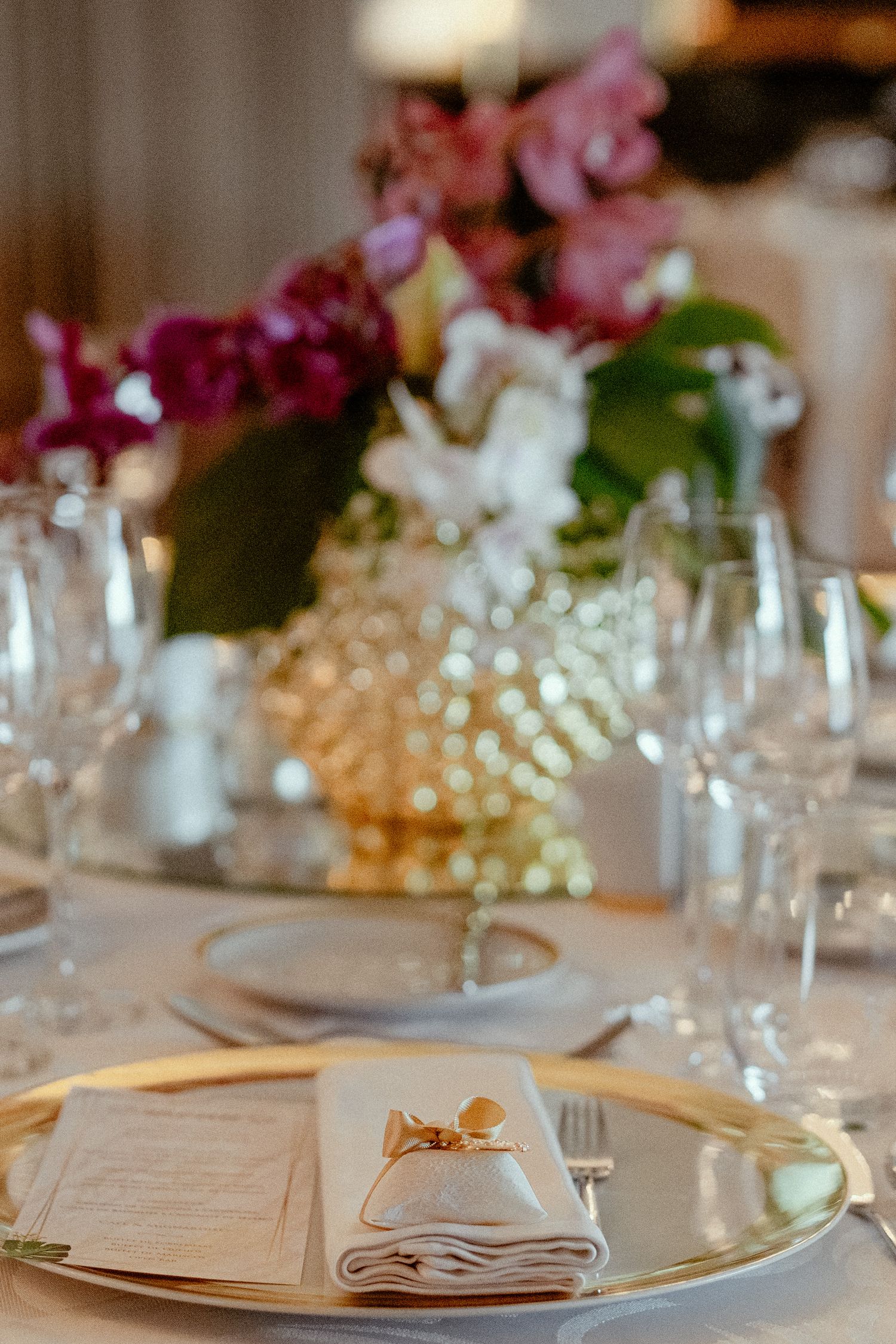 Elegant table settings with gold charger plates, white dishes, and pink floral centerpieces create a romantic wedding atmosphere.