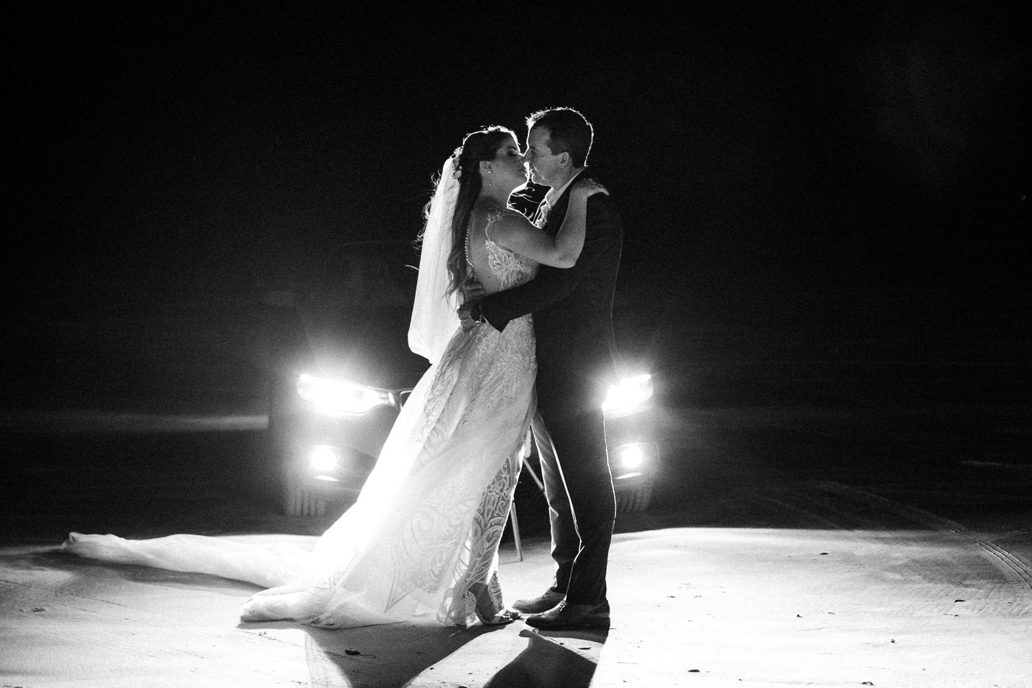 A dance couple in elegant formal attire performs graceful dance moves on a dark stage illuminated by spotlights.