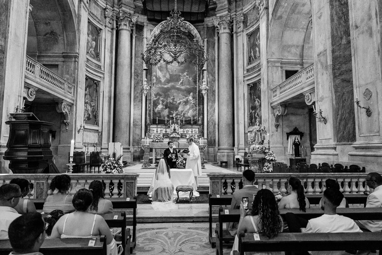 Black and white photo of a wedding ceremony at a grand church altar with guests seated in pews.