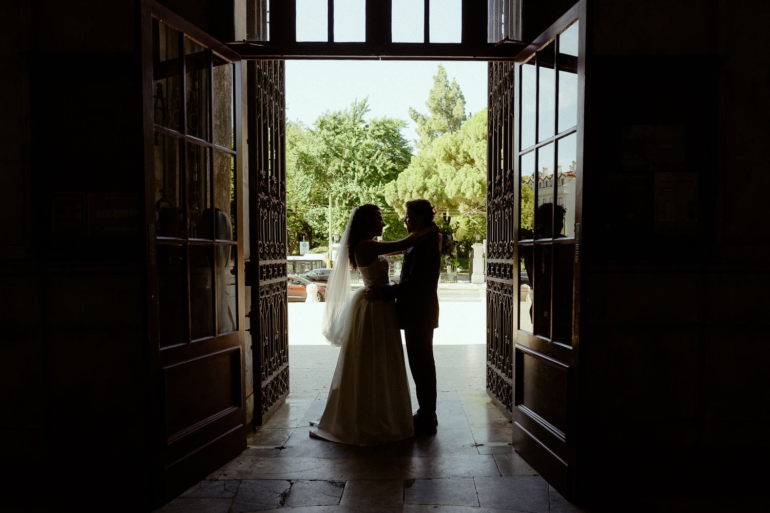 Silhouette of bride and groom embracing in elegant doorway with lush garden backdrop on their wedding day.