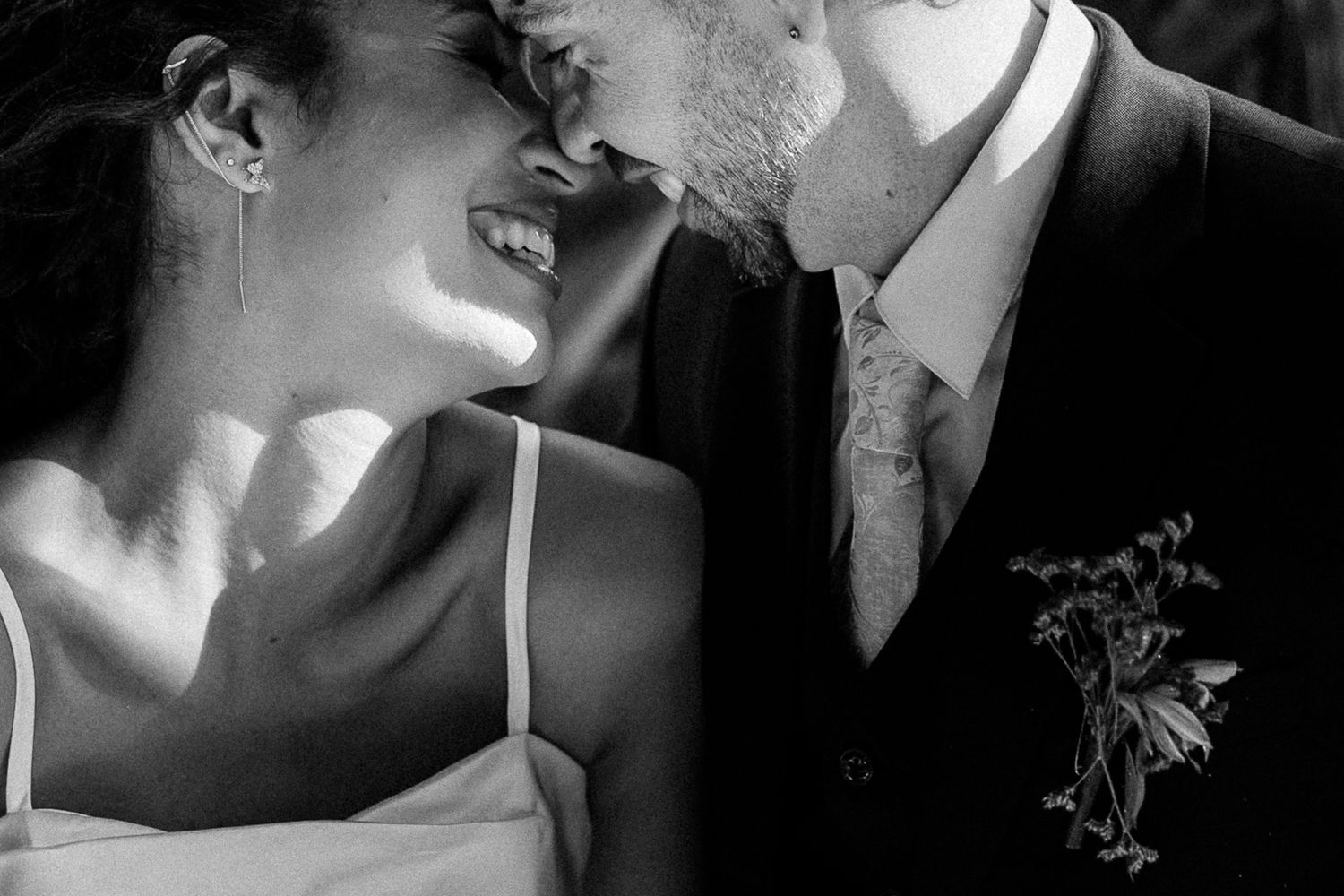 Black and white wedding photo of smiling bride and groom sharing an intimate moment, boutonniere visible.