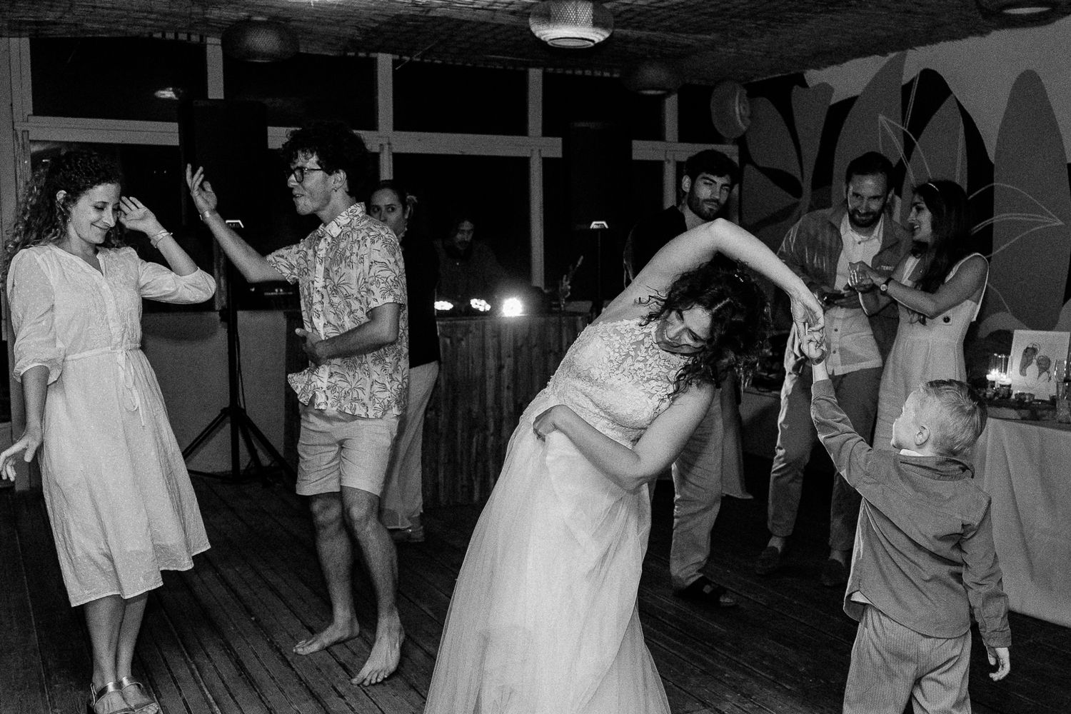 Black and white photo of bride dancing joyfully with guests at a wedding reception party.