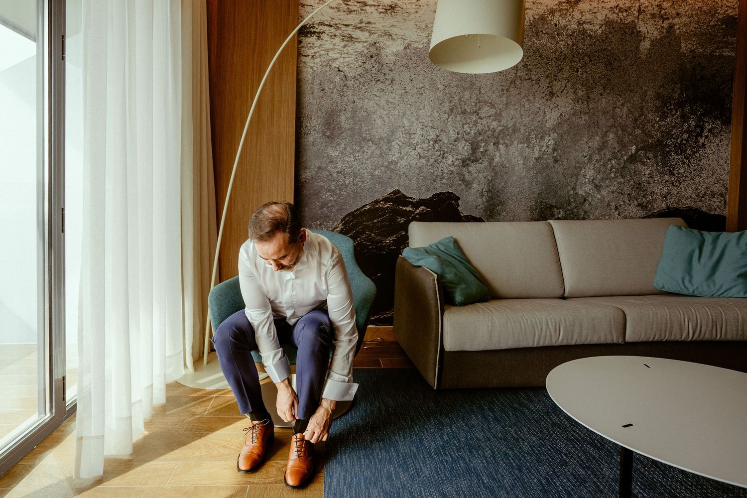 Modern living room interior with figure sitting by large window putting on shoes.