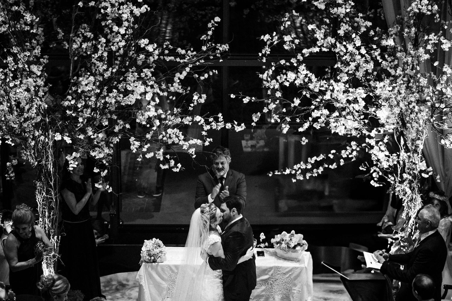 A nighttime wedding ceremony under illuminated trees with guests looking on.