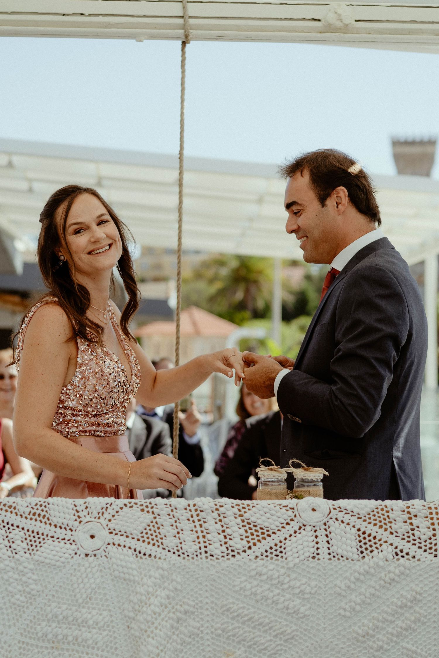 Couple shares a joyful moment at an outdoor reception with lace tablecloth and drinks.