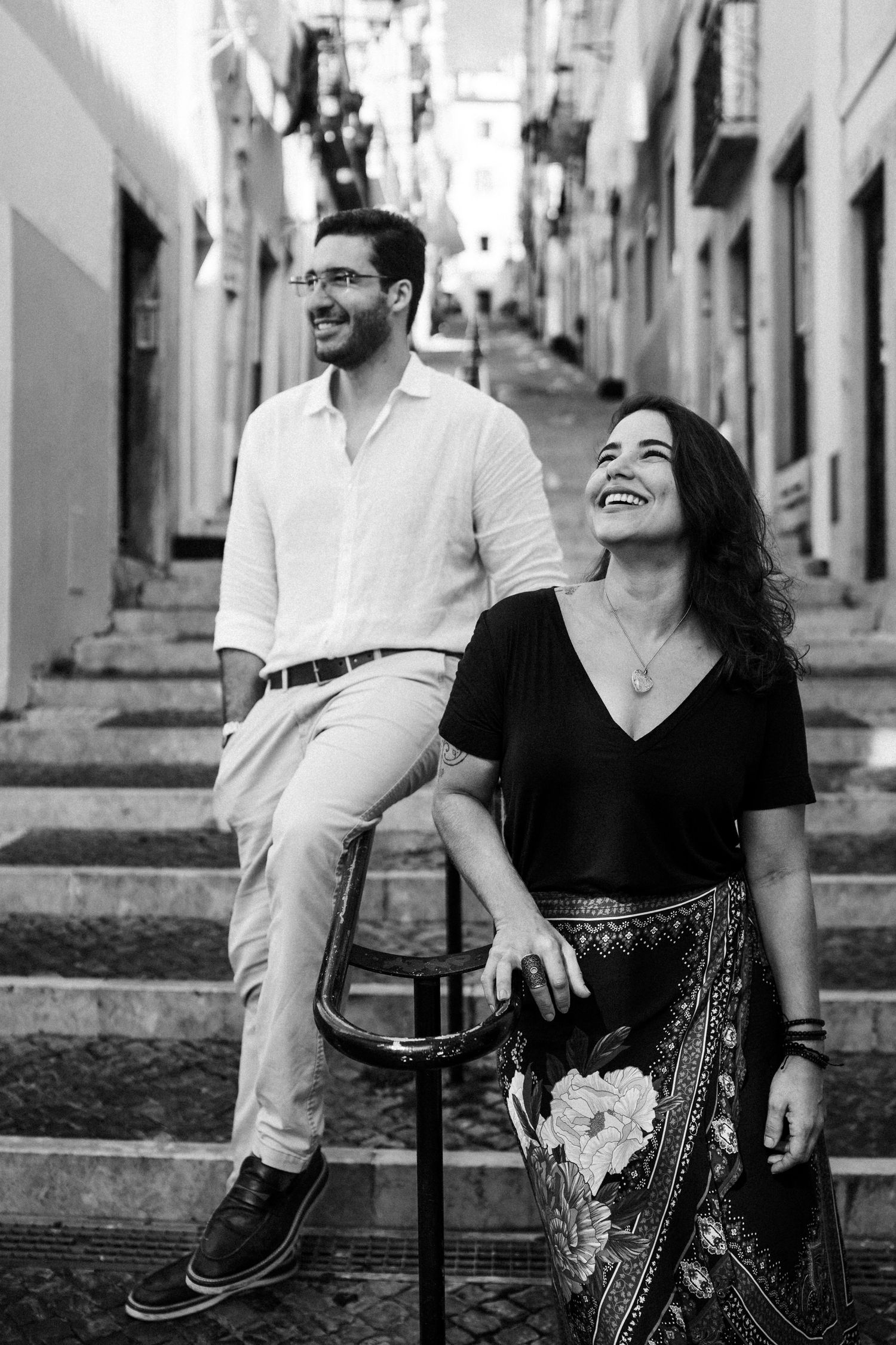 A couple shares a candid moment of laughter while sitting on stone steps in a narrow European alley.