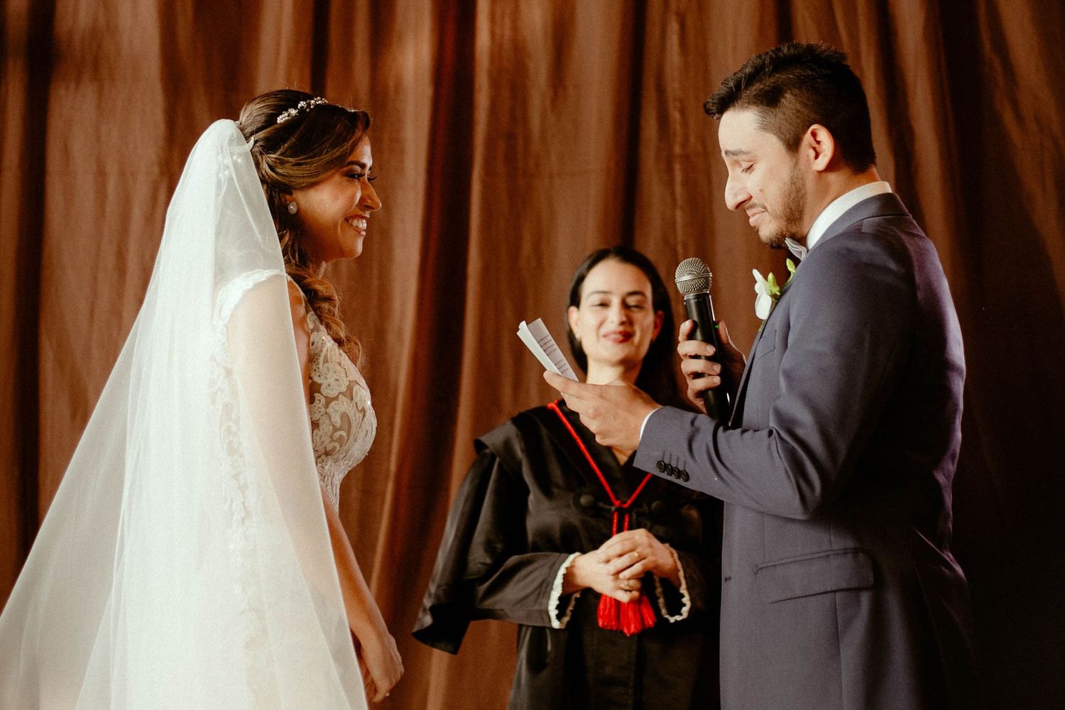 A wedding party stands in formal attire against a wooden wall during an indoor celebration ceremony.