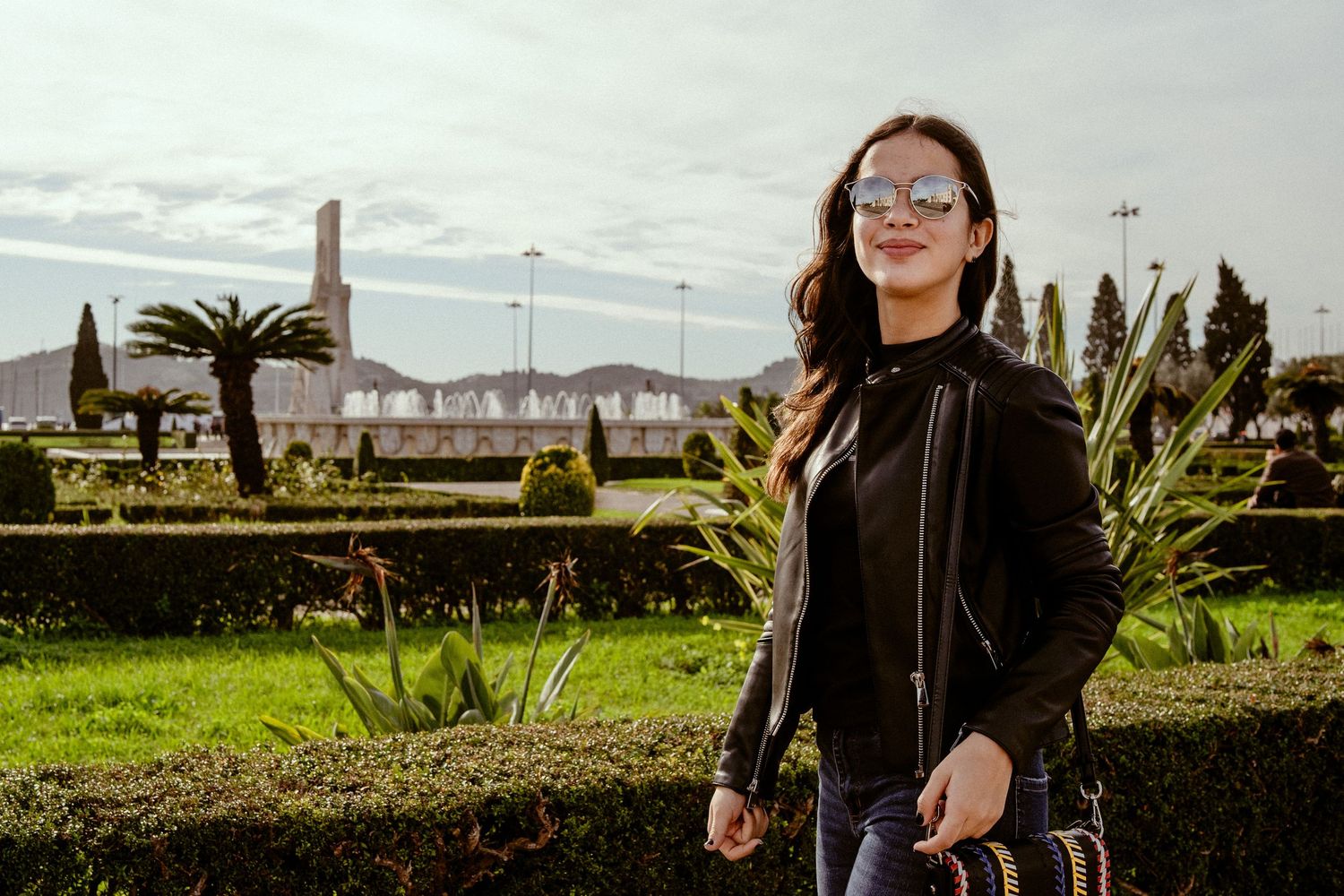Candid shot of person in leather jacket standing in garden with palm trees and greenery.