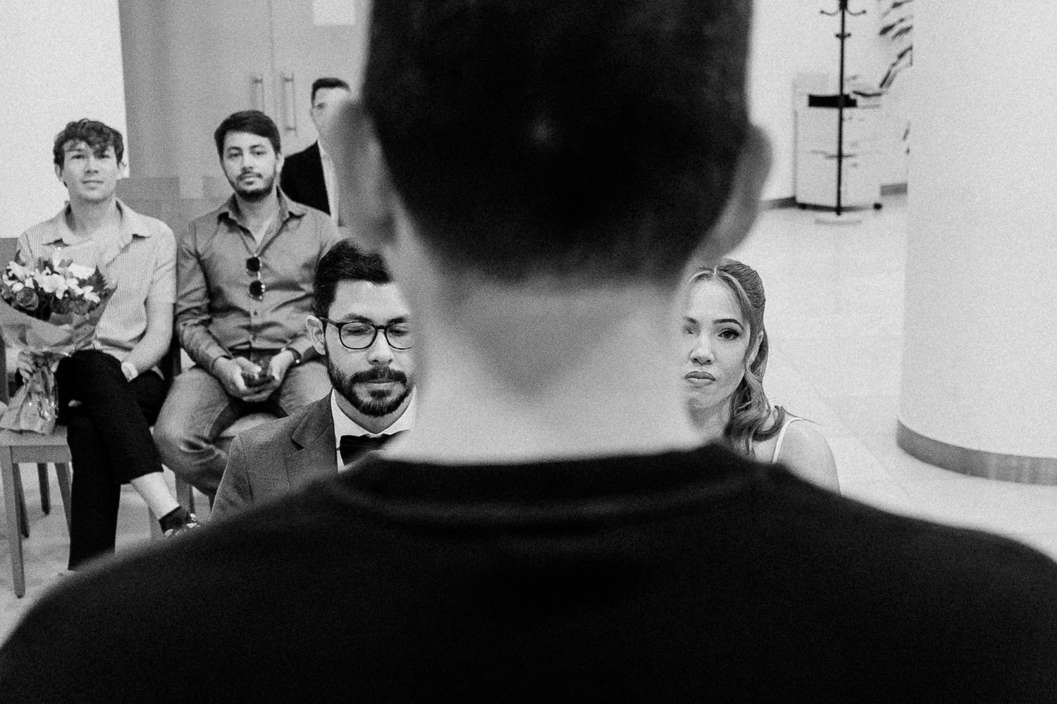 Black and white photo of people sitting in chairs listening to a speaker from behind in an indoor setting.