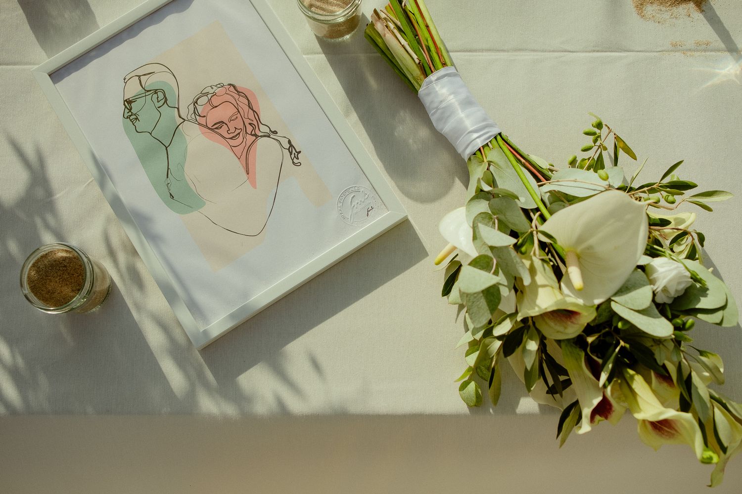 Elegant wedding flat lay with white calla lily bouquet, line art print, and gold ring on marble surface.
