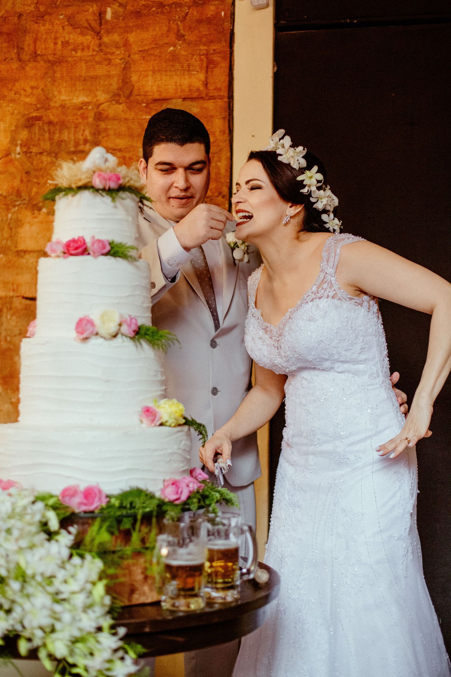 Playful moment of couple cutting their pink-decorated wedding cake.