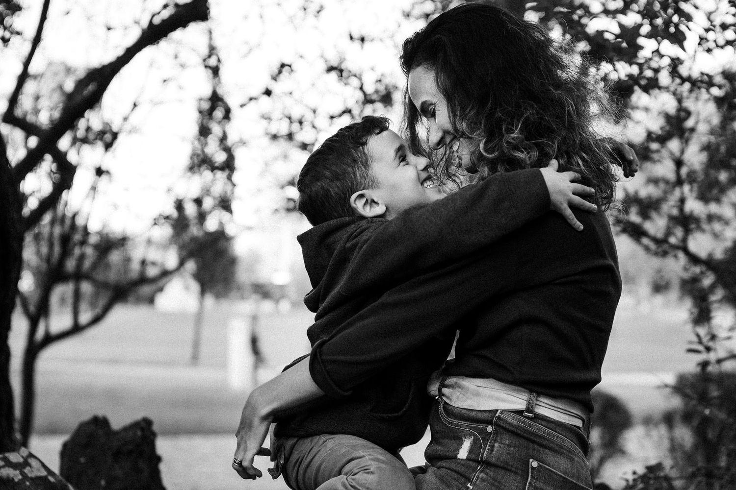 A tender black and white photograph captures an intimate embrace between two people outdoors in a park-like setting.