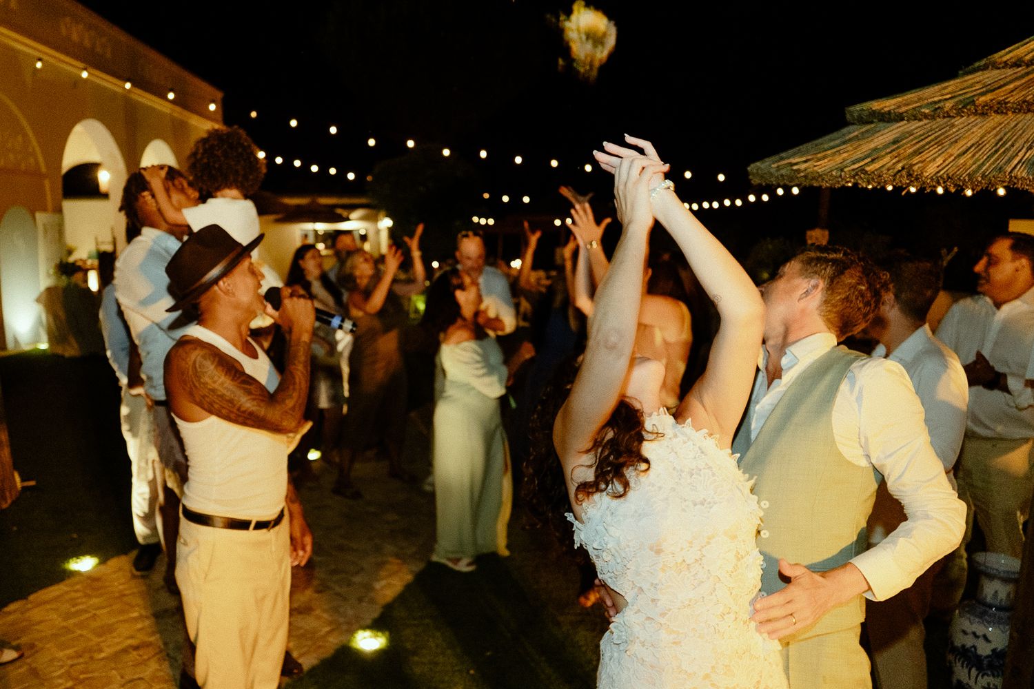Bride and groom share first dance surrounded by cheering guests under string lights at outdoor wedding reception.