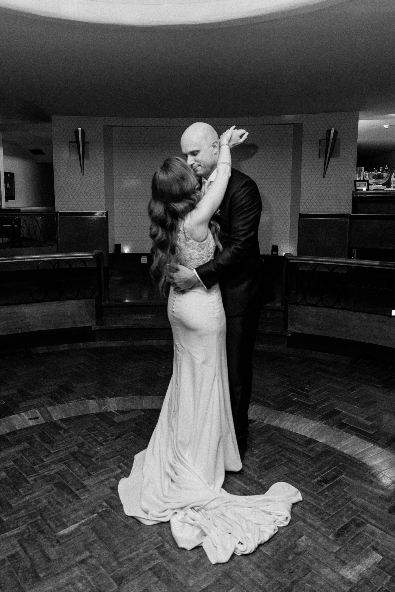 Bride and groom share intimate first dance embrace in black and white wedding photo on dance floor.