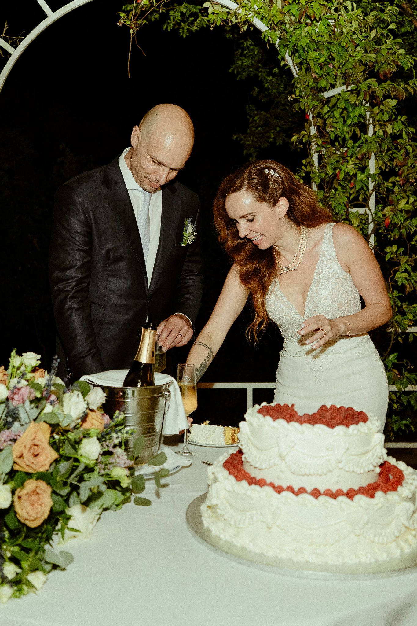 Bride and groom cutting a white wedding cake decorated with fresh raspberries at their reception.