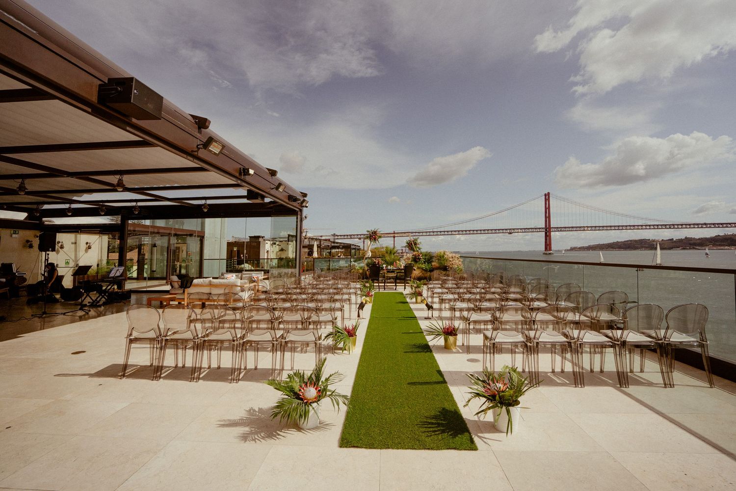 Wedding ceremony setup on an oceanfront deck with white chairs and green grass aisle runner against dramatic cloudy sky.