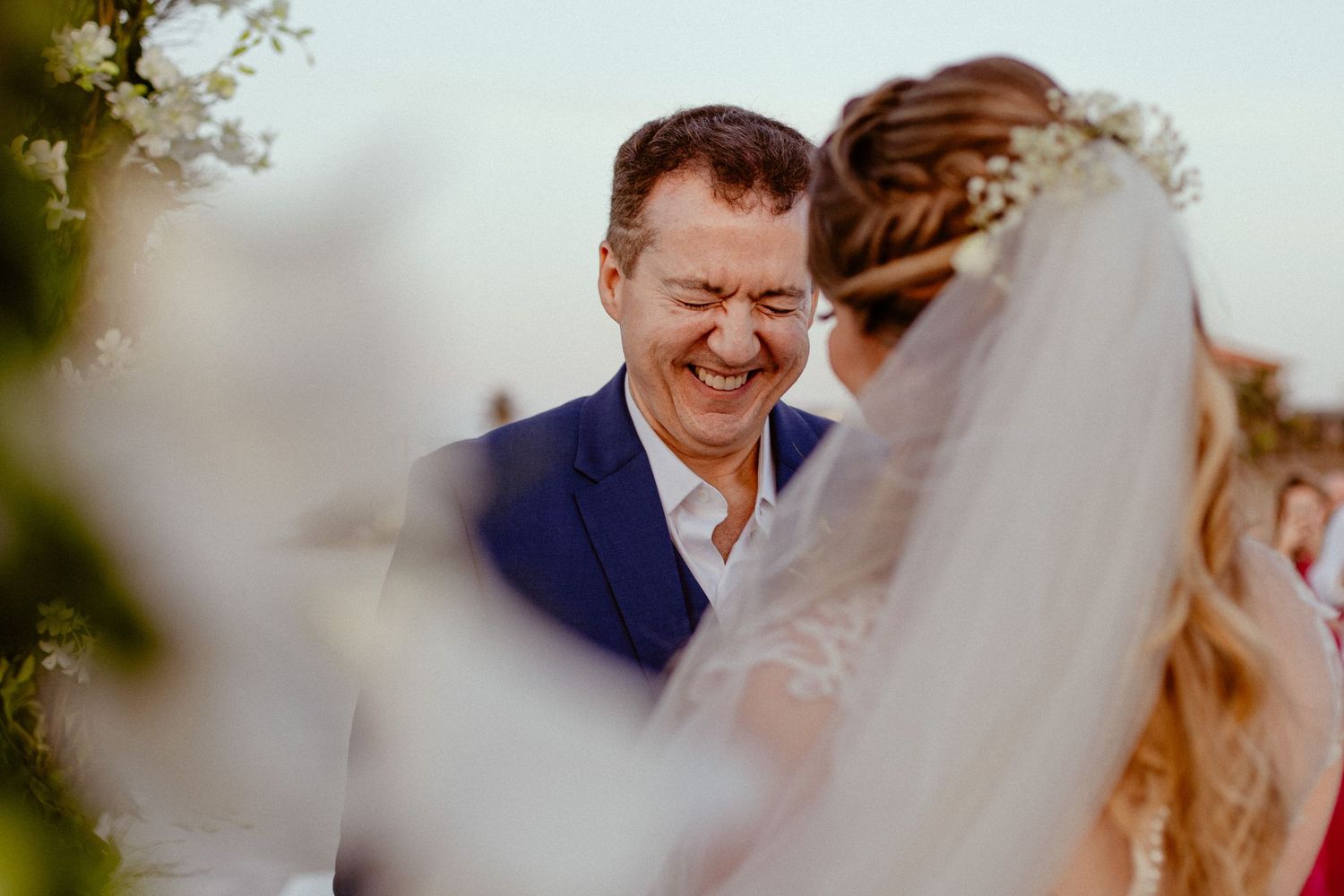 A bride and groom share a joyful laugh during their outdoor wedding ceremony in natural lighting.