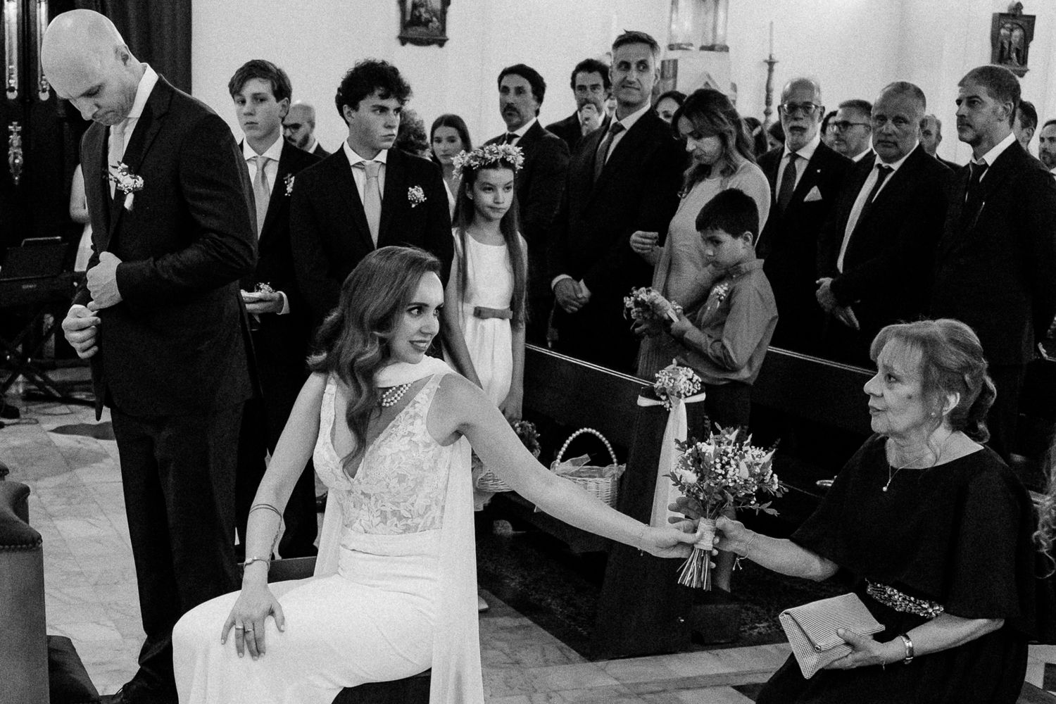 Black and white wedding ceremony photo of bride in white gown with guests and flower girl in church.