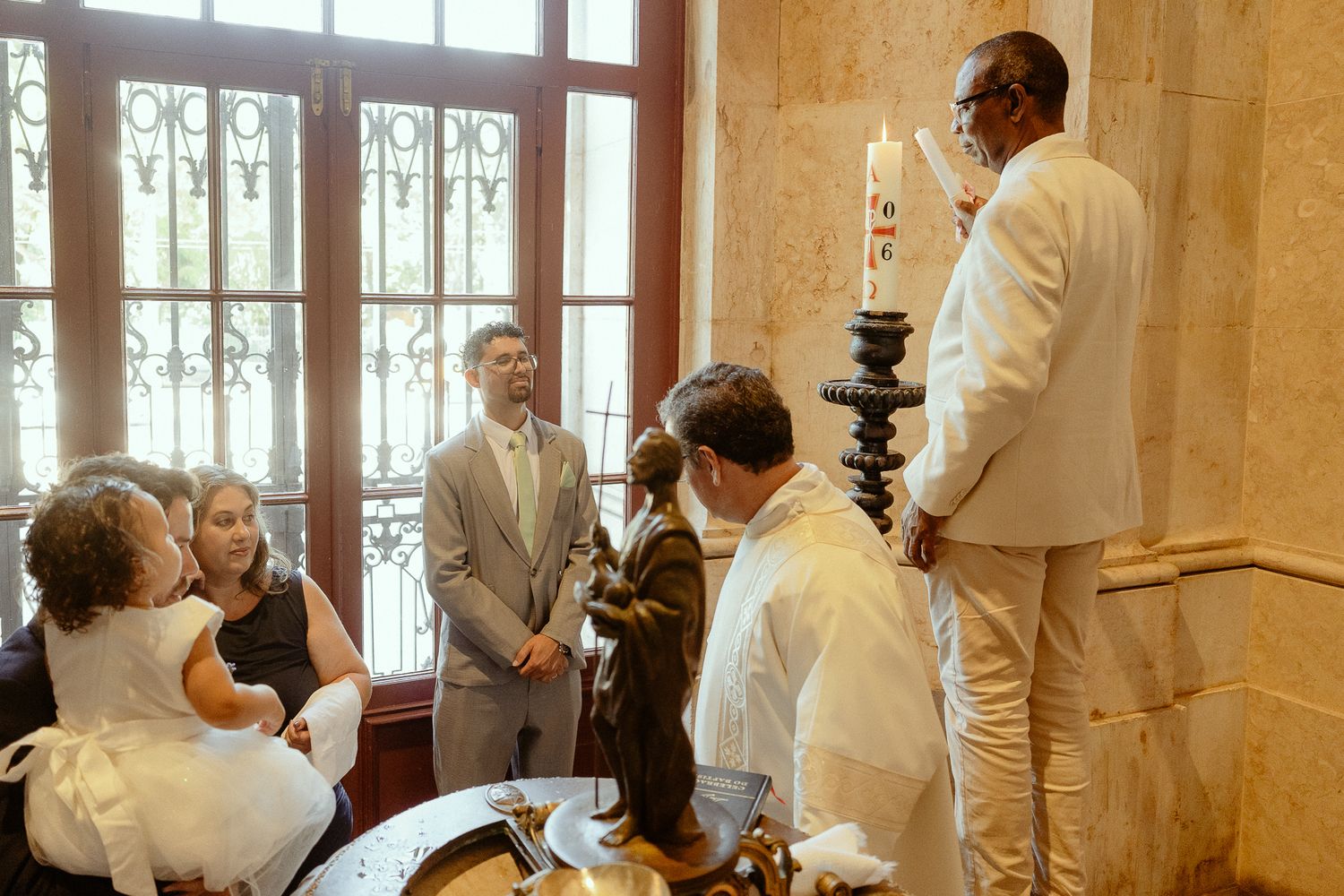 Wedding ceremony gathering with guests in elegant attire inside a classic venue with ornate windows.