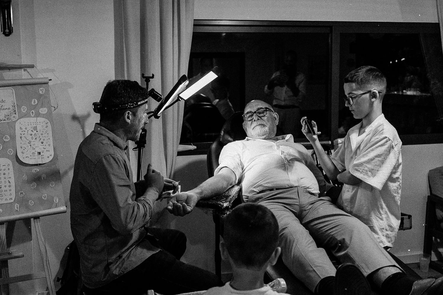 Black and white photo of three men in a room, one seated relaxing while others engage in conversation nearby.