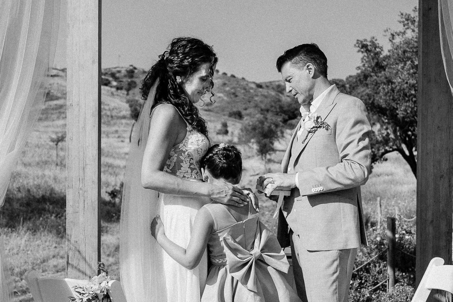 Black and white photo of a bride and groom exchanging vows at an outdoor wedding ceremony.