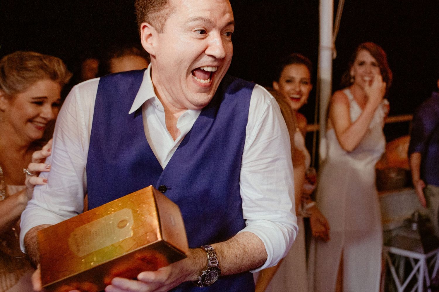 Joyful guest at a wedding reception reacts excitedly while holding up a gift or package.