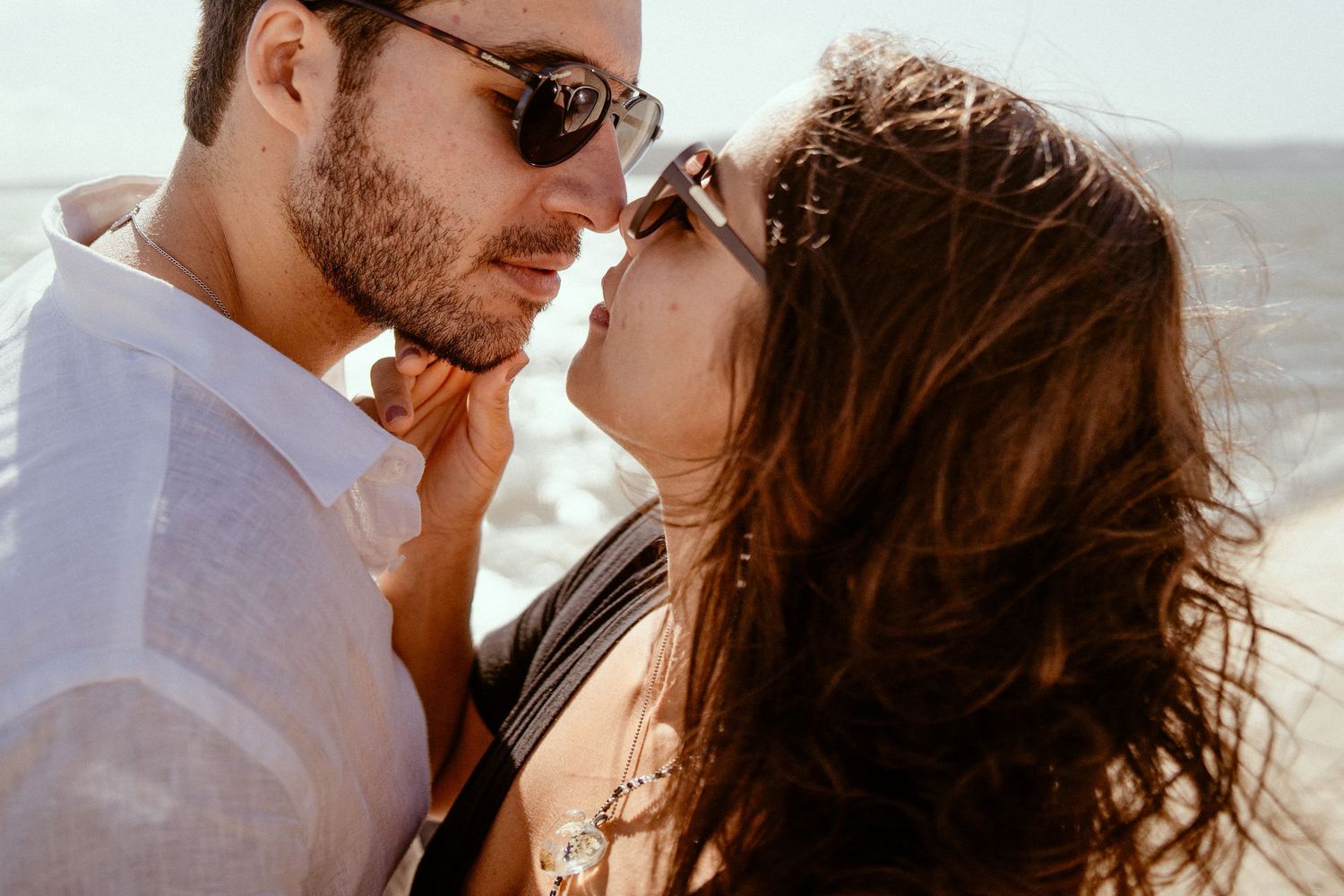 Close up romantic photo of a couple about to kiss, with sunlight behind them and a white shirt glowing in natural light.