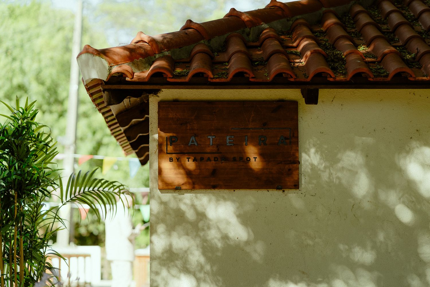 Rustic wooden cafe sign mounted on a white stucco wall with terracotta roof tiles and tropical greenery.