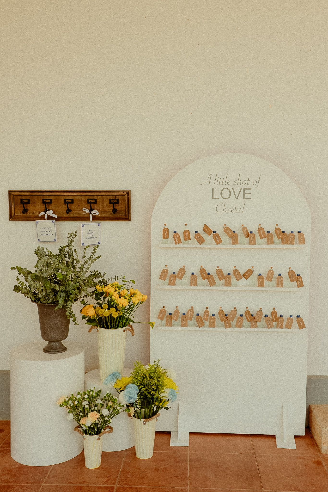 Wedding shot bar display with white arch board, mini bottles, and floral arrangements in yellow and green.