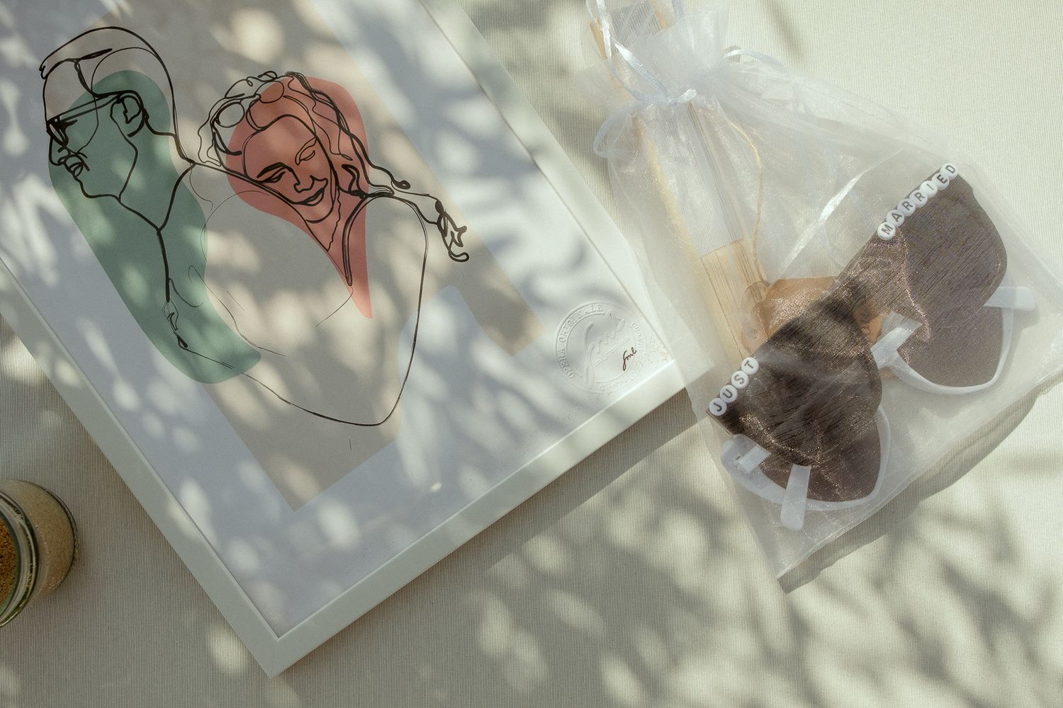 Wire art print of a woman and a bagged teddy bear charm on a sunlit surface with dappled shadows.