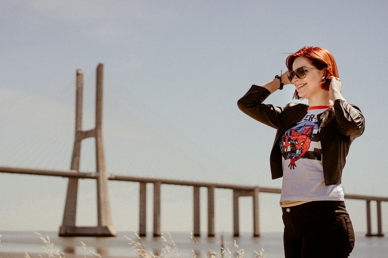 A figure in a leather jacket and graphic tee poses against a bridge backdrop with dramatic lighting.