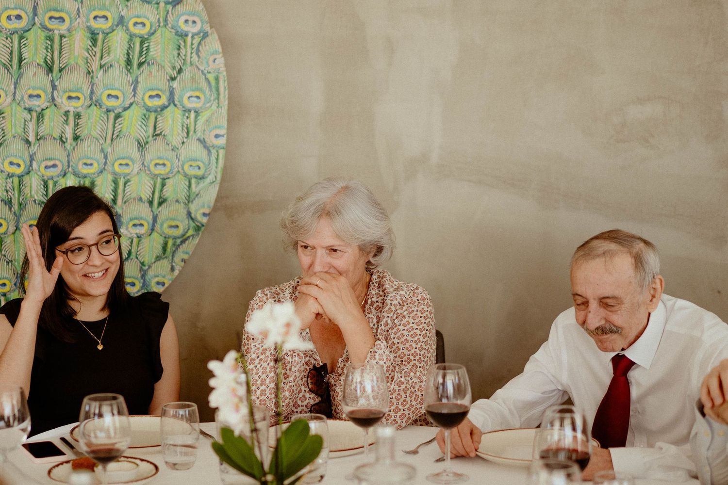 People seated at a long dining table in a restaurant setting with decorative green wallpaper in the background.