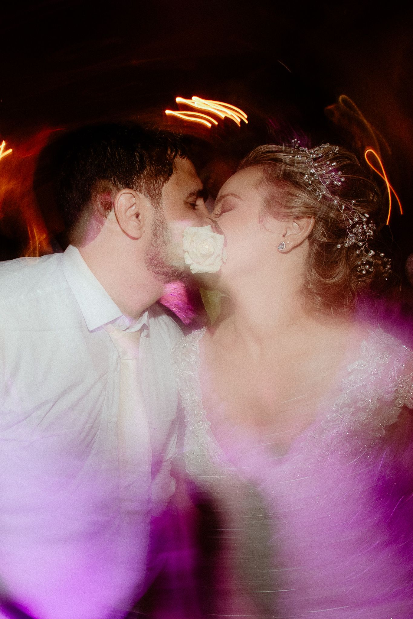 A romantic wedding couple shares their first kiss in a dreamy purple-lit atmosphere during their reception.