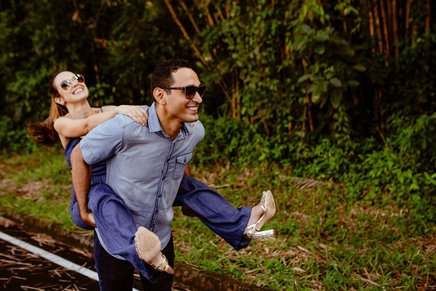 Two people play and laugh together while balancing on train tracks in a forest setting.
