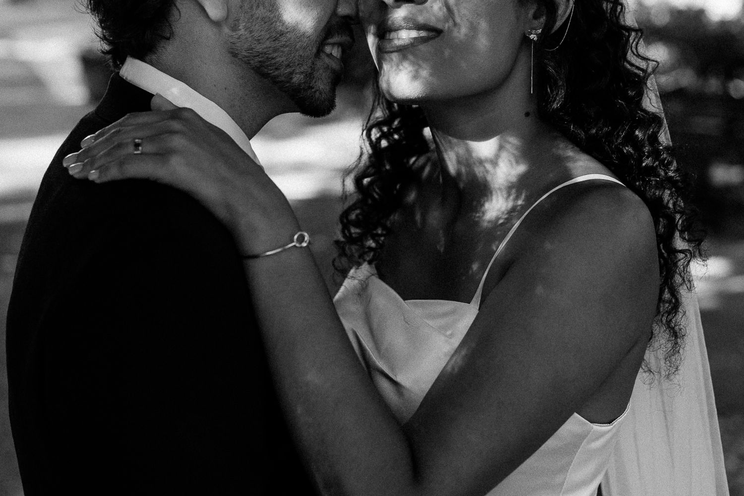 Black and white wedding photo of a couple in an intimate embrace, bride in white dress with curly hair, groom in dark suit.